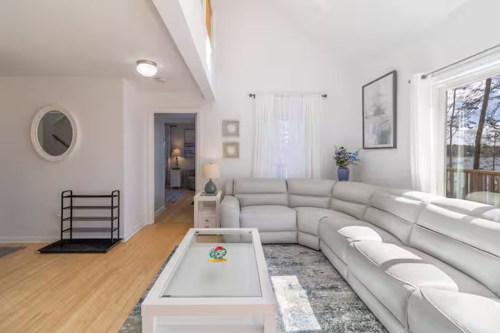 Bright living room with white sectional sofa, coffee table, wood floors, and large windows