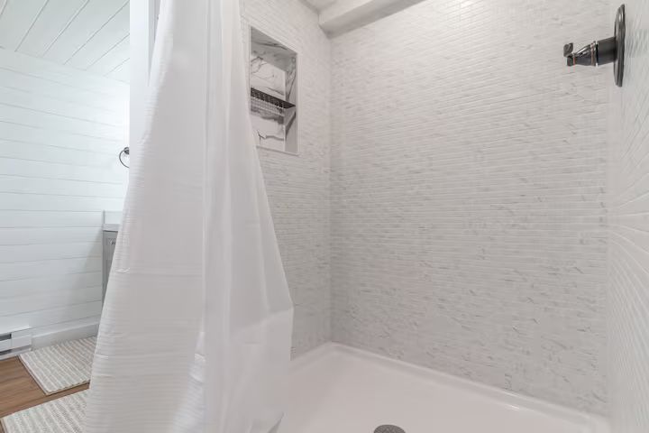 White shower stall with textured walls, a shower curtain, built-in niche, and wall-mounted fixture