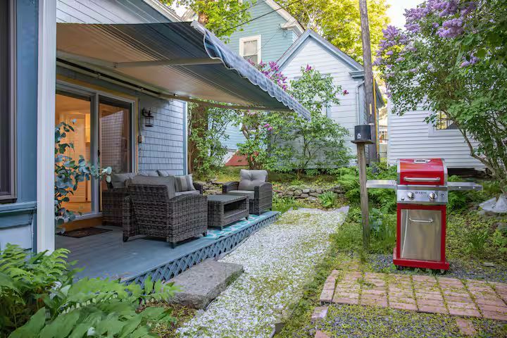 Backyard patio with wicker seating, stone path, and red grill beside a house