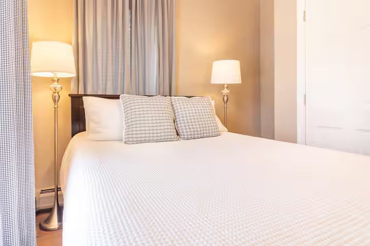 Cozy bedroom with a white bed, striped pillows, and warm floor lamps beside curtains