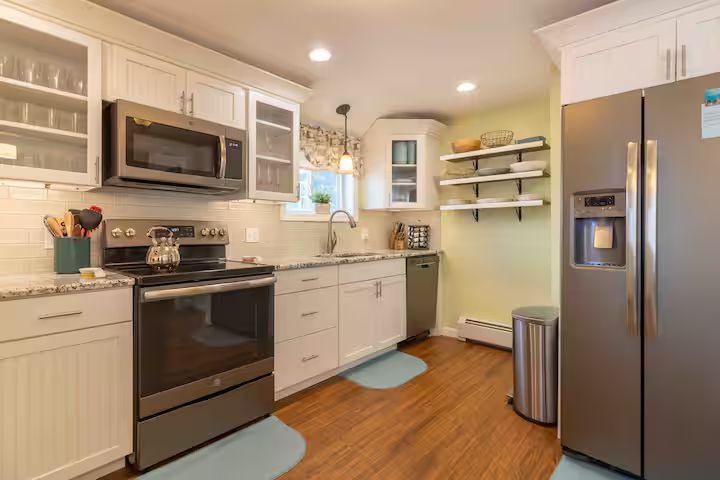 Bright modern kitchen with stainless steel appliances, white cabinets, wood floor, and light blue rugs