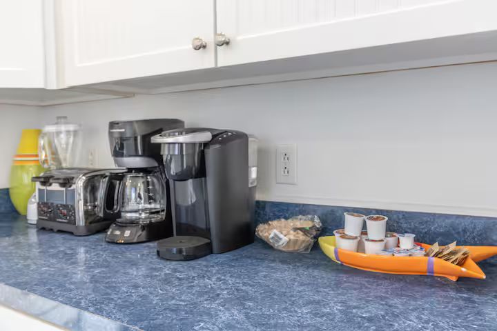 Kitchen counter with coffee maker, toaster, mugs, and an orange tray on a blue countertop.