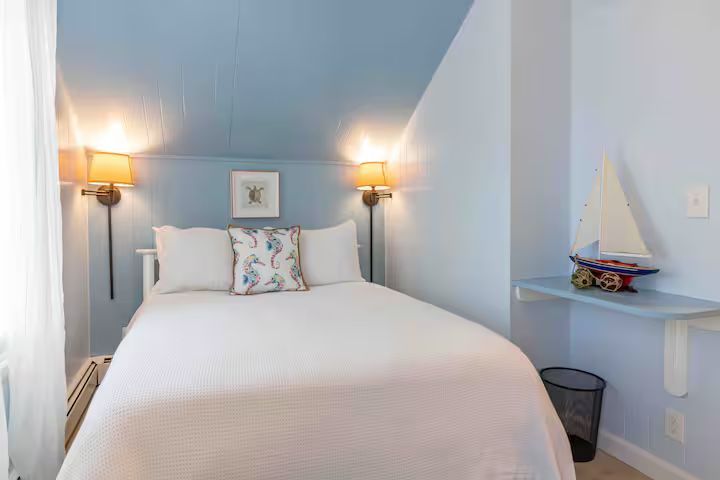Cozy twin bedroom with white bedding, blue walls, wall lamps, and a small shelf with decor