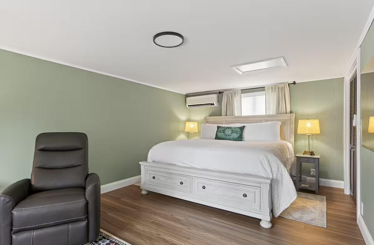 Bright bedroom with a white bed, green walls, wood floor, and a black recliner chair