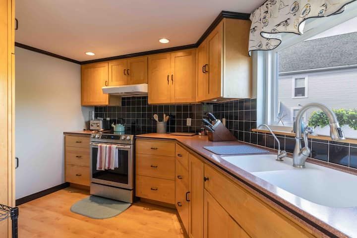 Modern kitchen with wooden cabinets, black tile backsplash, stainless stove, and large white sink countertop