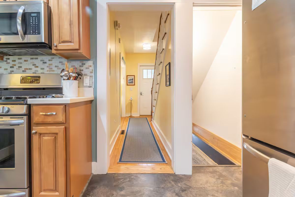Kitchen opening to a narrow hallway with wood trim, white walls, and a runner rug