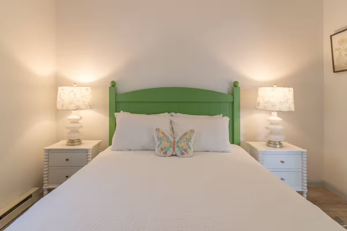 Bedroom with a green headboard, white bedding, and matching bedside lamps on each side.