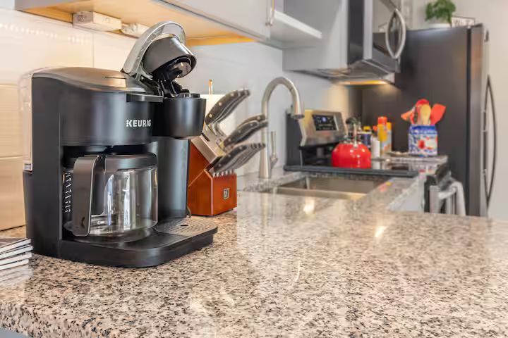 Kitchen counter with black coffee maker, granite countertop, sink, and stove in the background