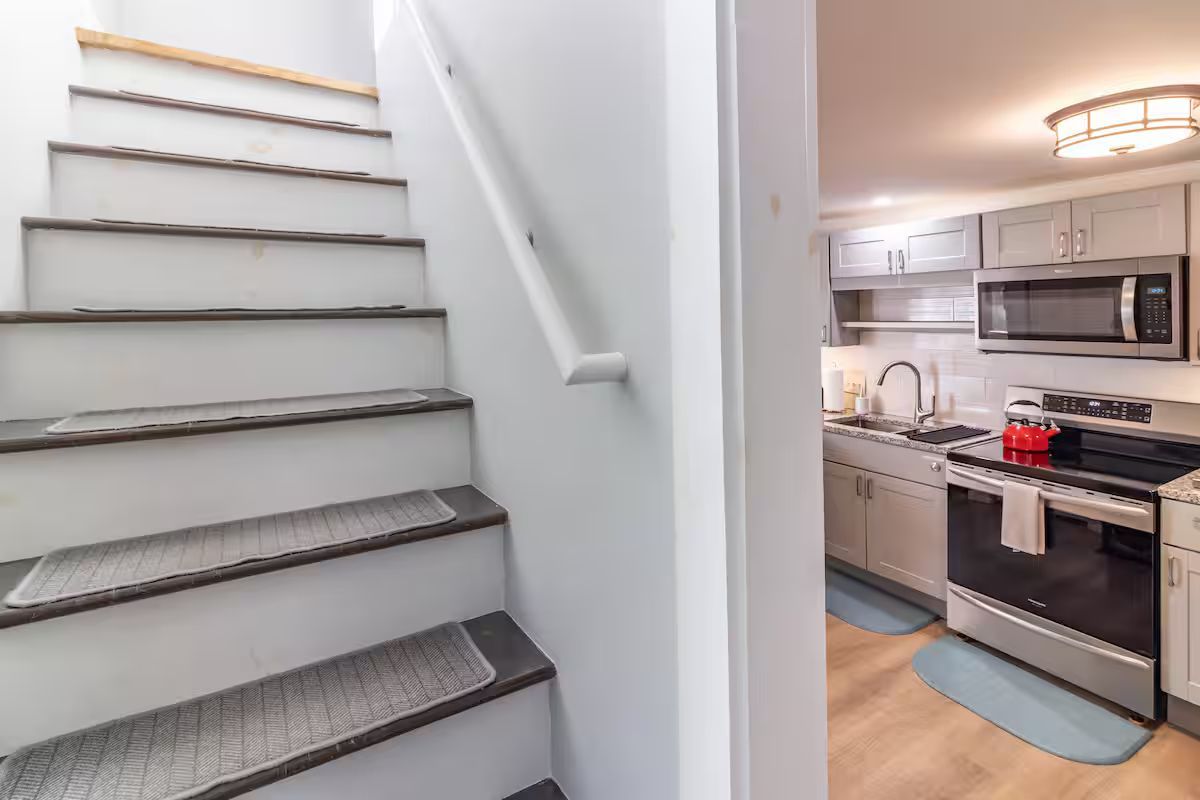 Stairway beside a modern kitchen with white cabinets, stainless steel appliances, and light wood floor