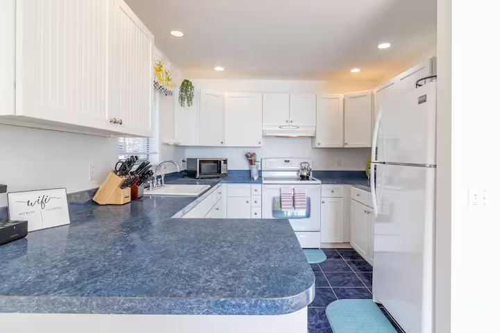Bright white kitchen with blue countertops, white cabinets, and a refrigerator on the right.