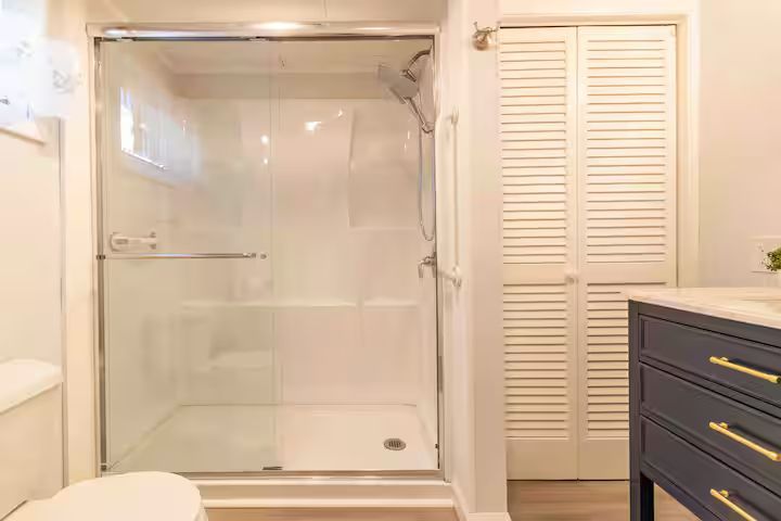 Bathroom with glass walk-in shower, white walls, and dark vanity with gold handles