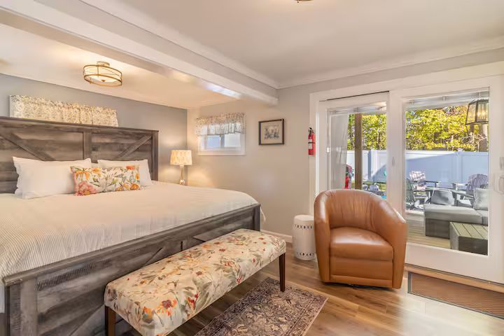 Bright bedroom with king bed, floral bench, tan chair, and glass doors to a patio