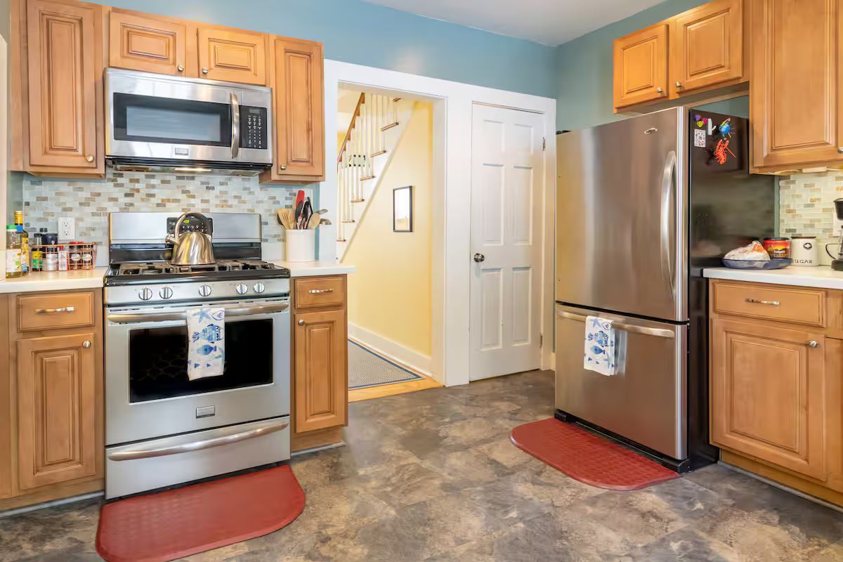 Modern kitchen with stainless steel appliances, wood cabinets, and gray tile flooring
