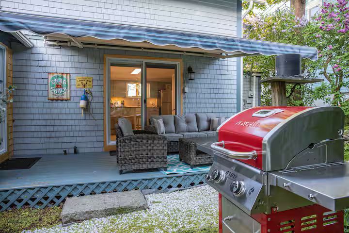 Patio with wicker chairs and red grill outside a gray house with a covered awning