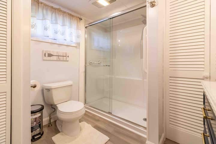 Small beige bathroom with toilet, vanity, and glass-enclosed shower