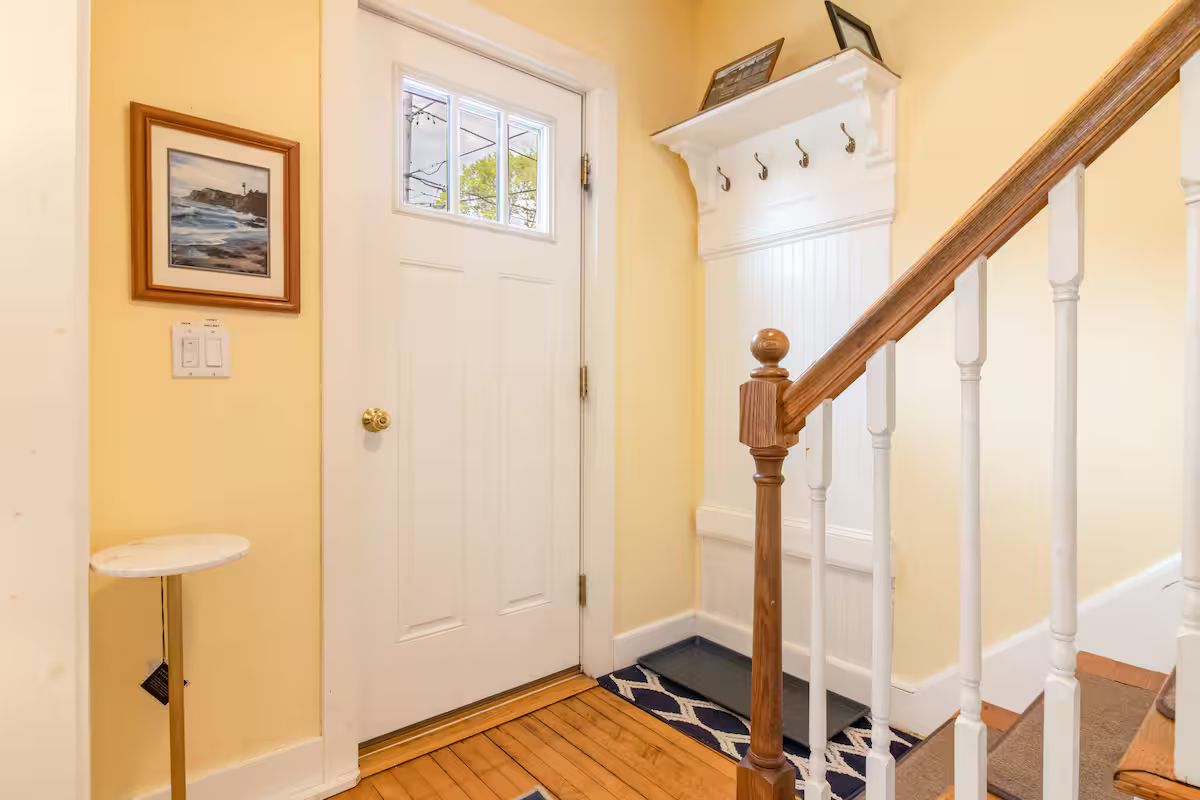 Bright entryway with white door, wood floor, staircase, and framed wall art