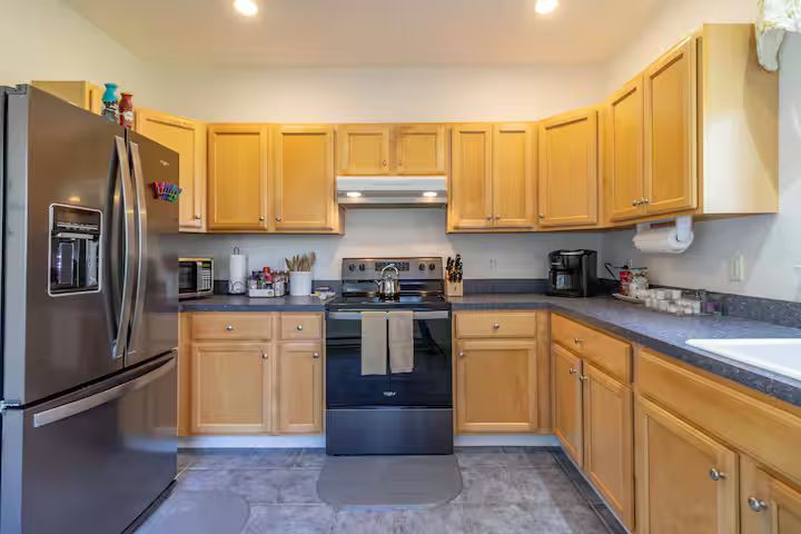 Modern kitchen with stainless steel appliances, light wood cabinets, and a gray tile floor