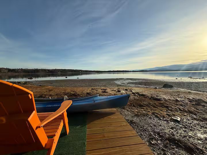 Orange chair on a wooden dock overlooking a calm shoreline at sunset.