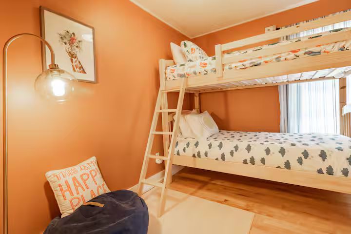 Cozy orange bedroom with loft bed, ladder, floor cushion, and window light