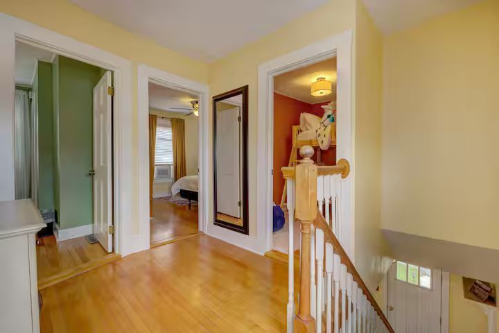 Bright hallway with hardwood floors, white trim, mirror, and open doorways in a warmly lit home