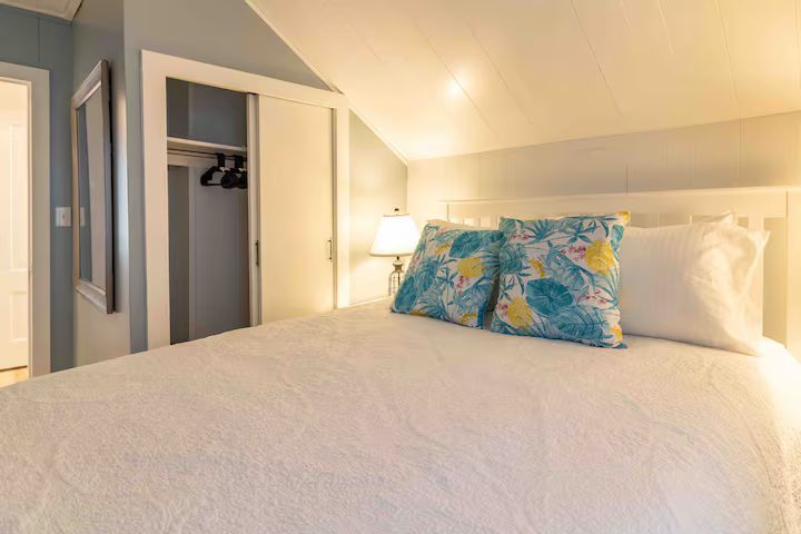Bright bedroom with white bed, blue floral pillow, and open closet door