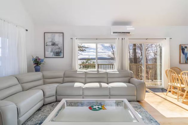 Bright living room with a sectional sofa, glass coffee table, and large windows overlooking a waterfront view