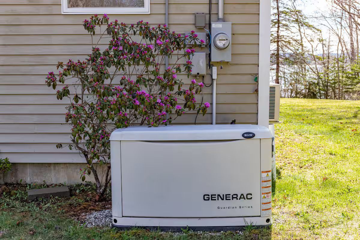 Generac home backup generator beside a house with flowering shrub and utility meter