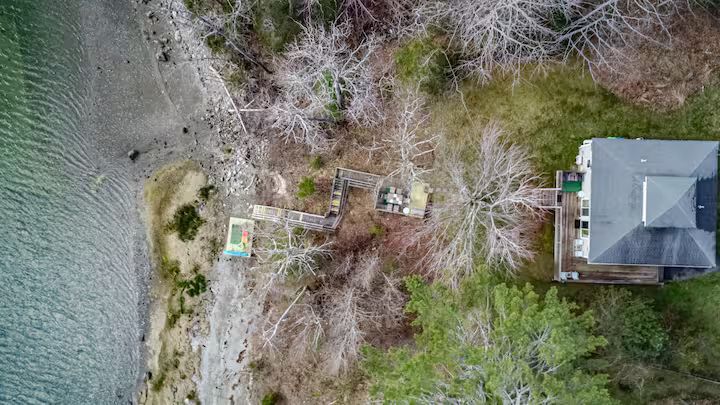 Aerial view of a lakeside dock area beside a house with trees and shoreline.