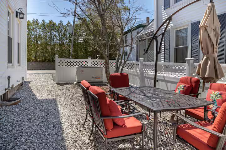 Gravel patio with red-cushioned dining set, umbrella, and white lattice fence beside a house