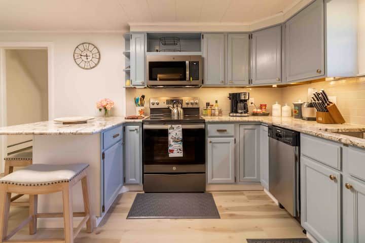 Bright kitchen with blue-gray cabinets, stainless appliances, white countertops, and a small dining nook