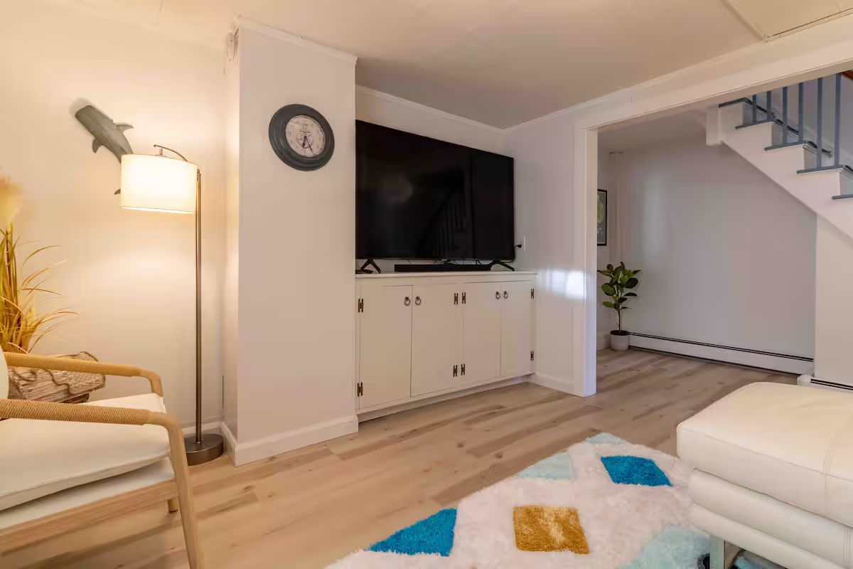 Modern living room with wall-mounted TV, white sofa, and staircase leading up.