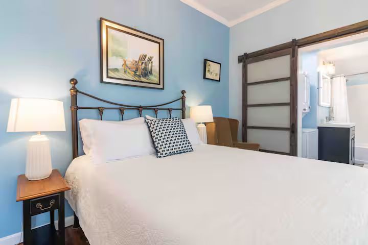 Bright bedroom with a white bed, blue walls, bedside lamps, and a sliding barn door to a bathroom