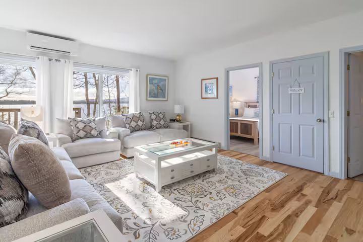 Bright, airy living room with a white sofa, patterned rug, coffee table, and hardwood floors.