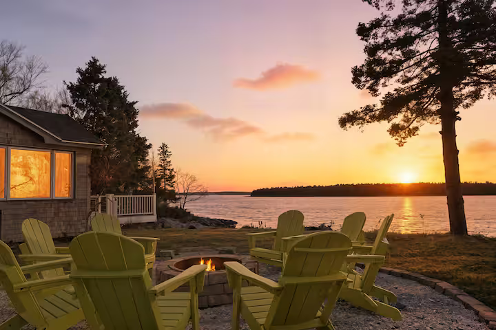 Lakeside cabin at sunset with Adirondack chairs on the shore and glowing orange sky