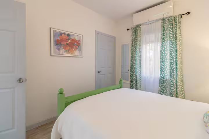 Bright bedroom with a green bed, white walls, framed art, and patterned curtains