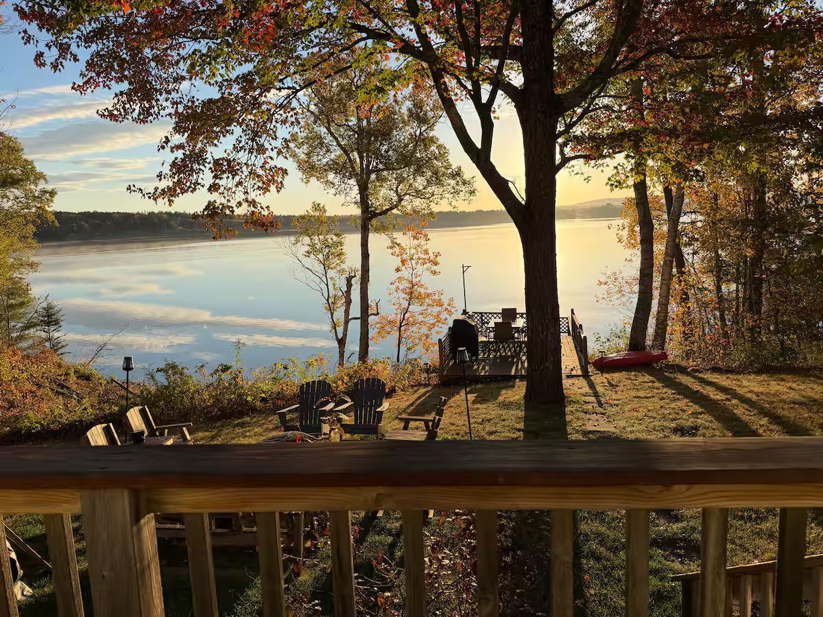 Wooden deck overlooking a calm lake at sunset, with autumn trees and a person sitting by the water.