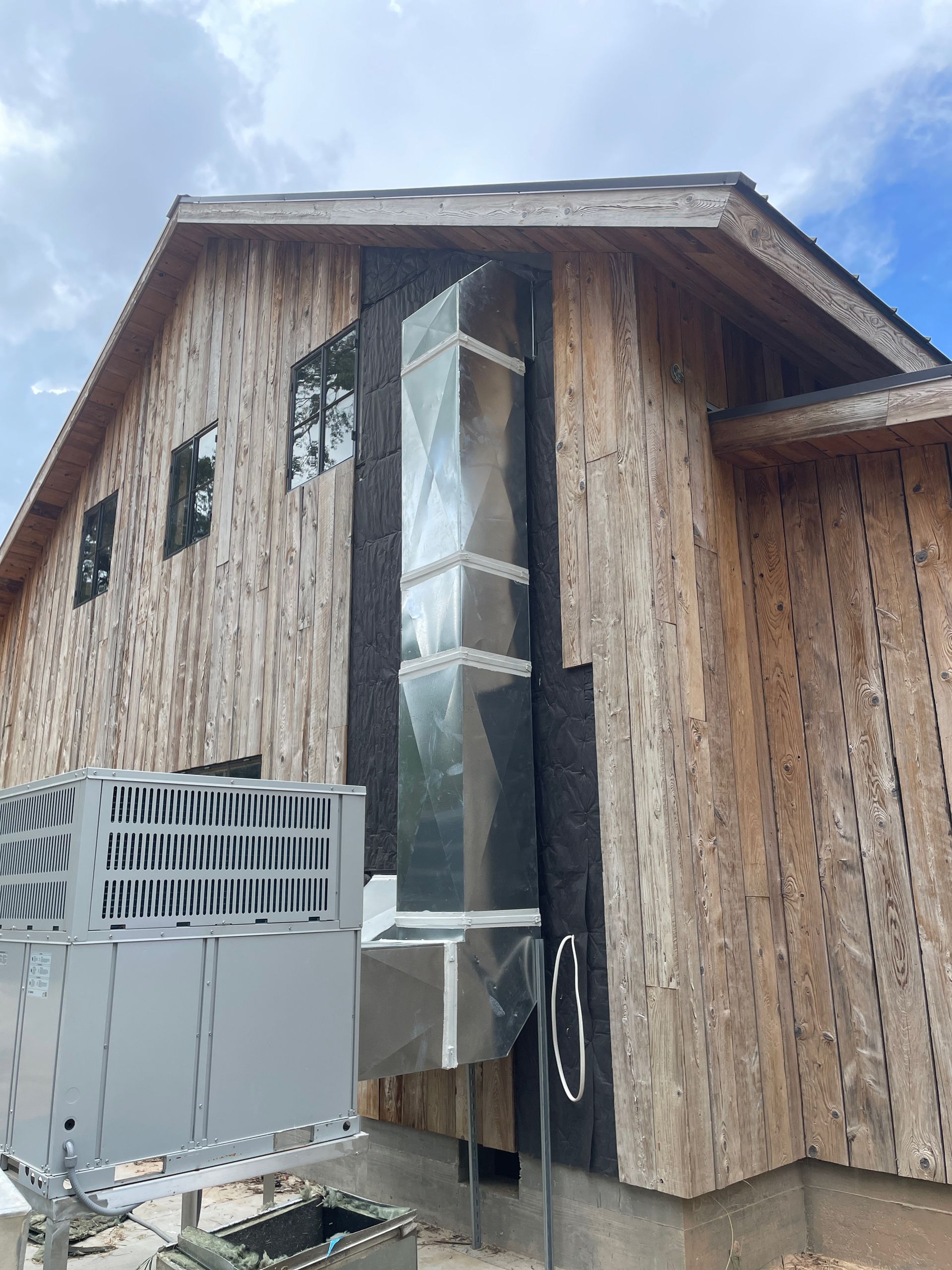 Damaged wooden house with a torn metal chimney vent and snowy roof under cloudy sky