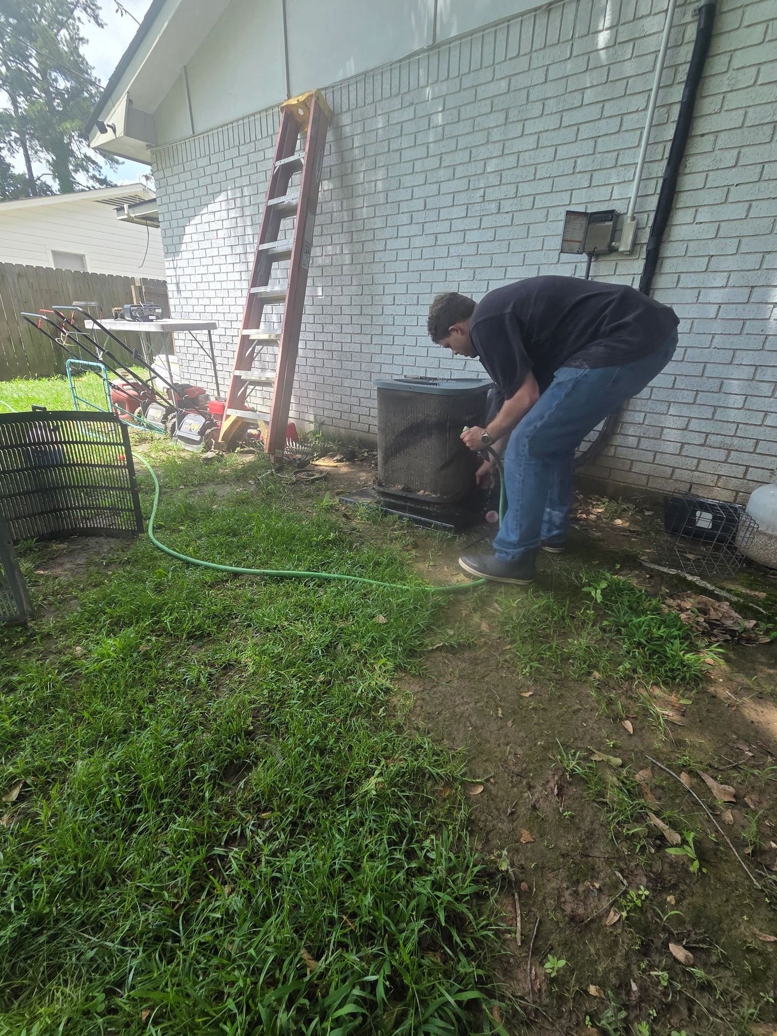 Person repairing a tire beside a white brick house in a grassy yard.