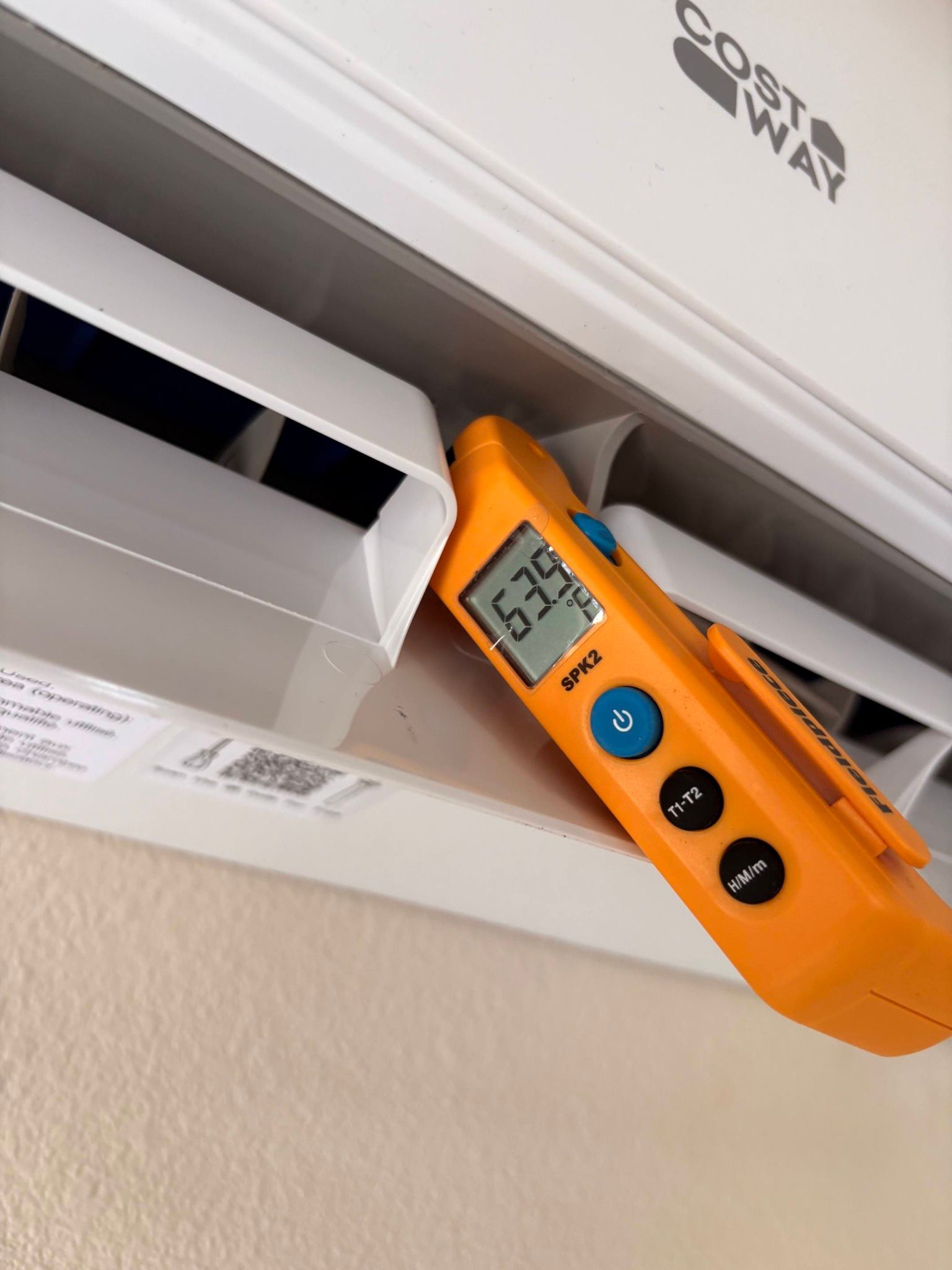 Orange detector measuring an air vent, displaying 53°F on a wall-mounted unit