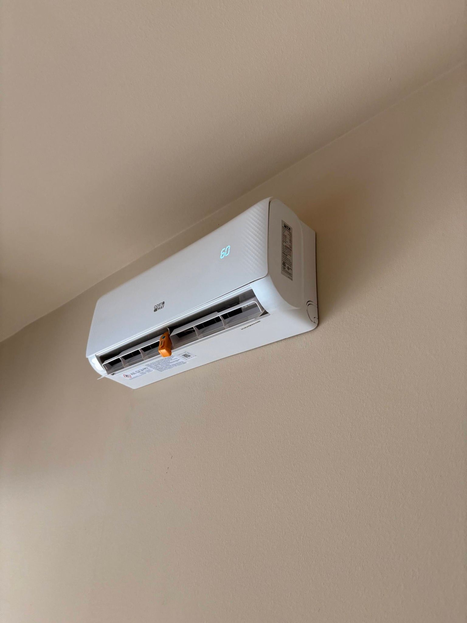 Wall-mounted white air conditioner near the ceiling on a beige wall.