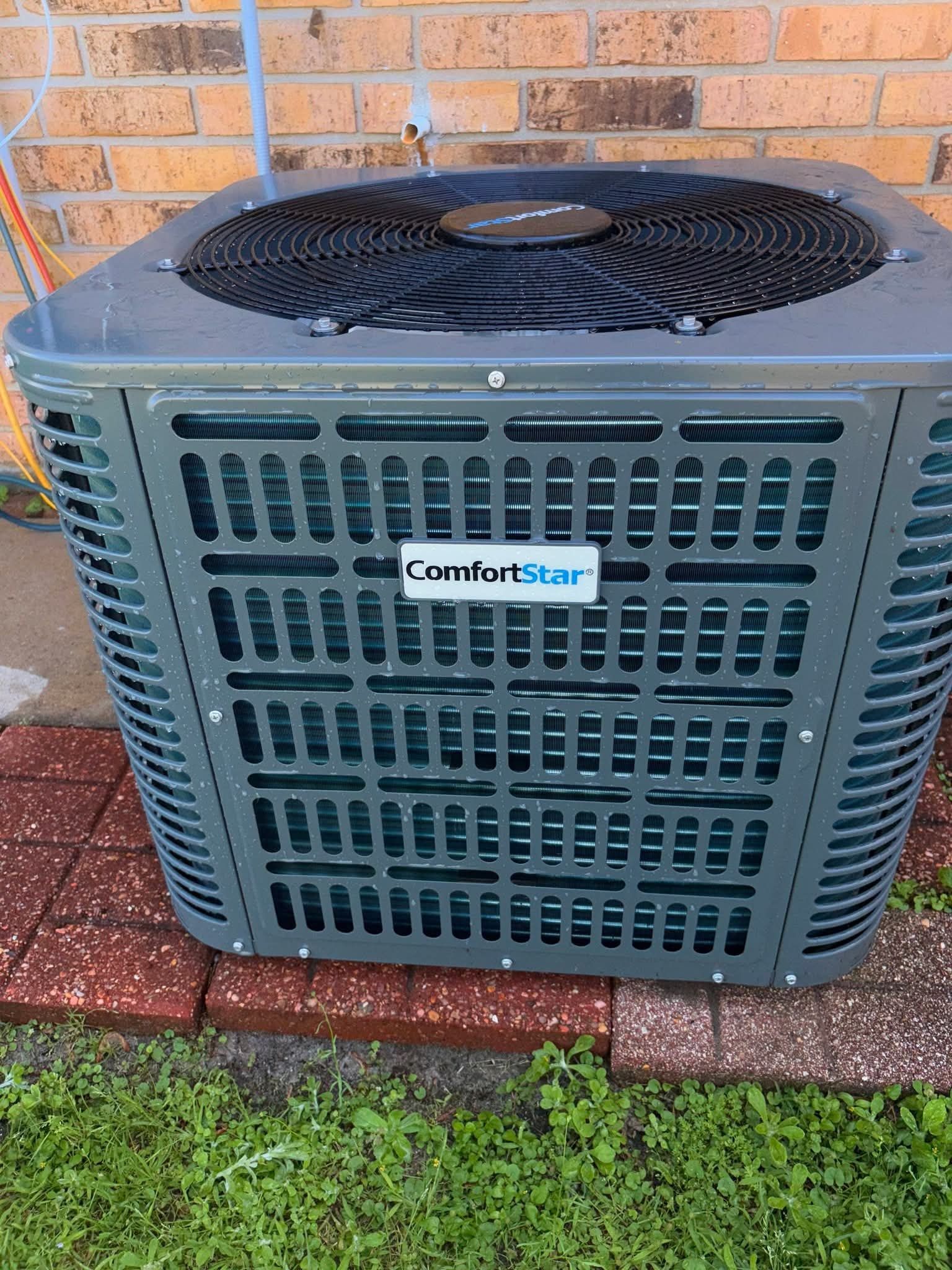 Outdoor ComfortStar air conditioner unit beside a brick wall and red pavers, with grass in front