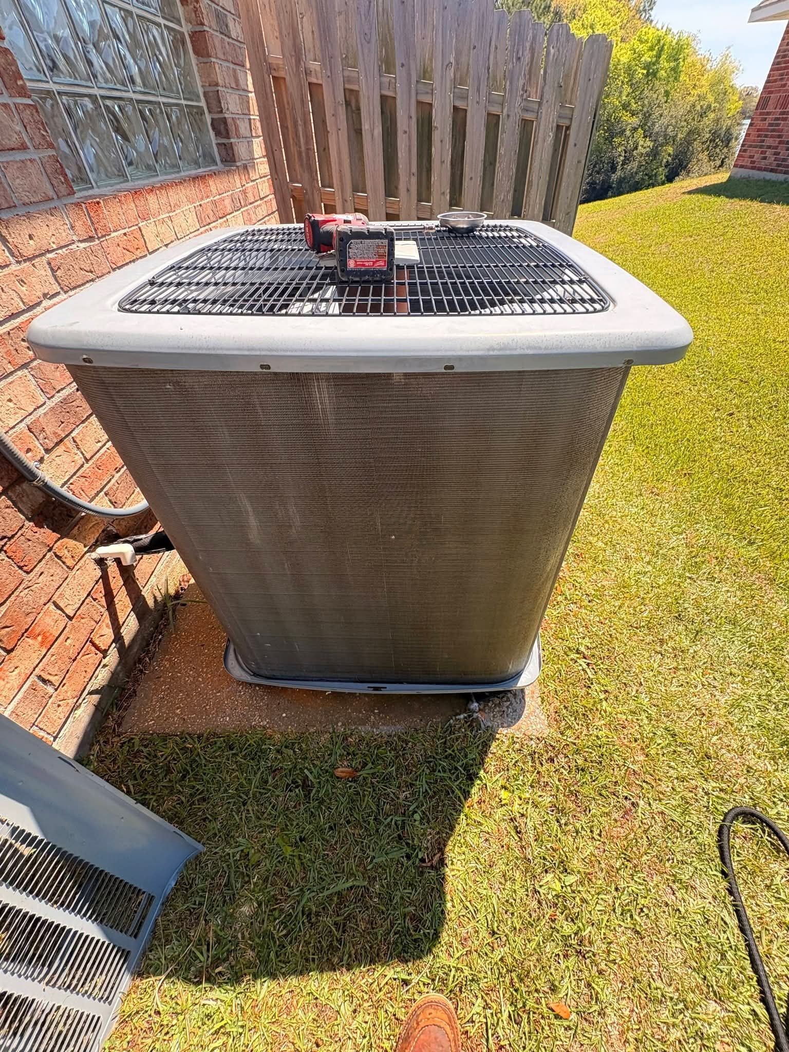 Outdoor air conditioner unit beside a brick house, with a red item on top and lawn around it
