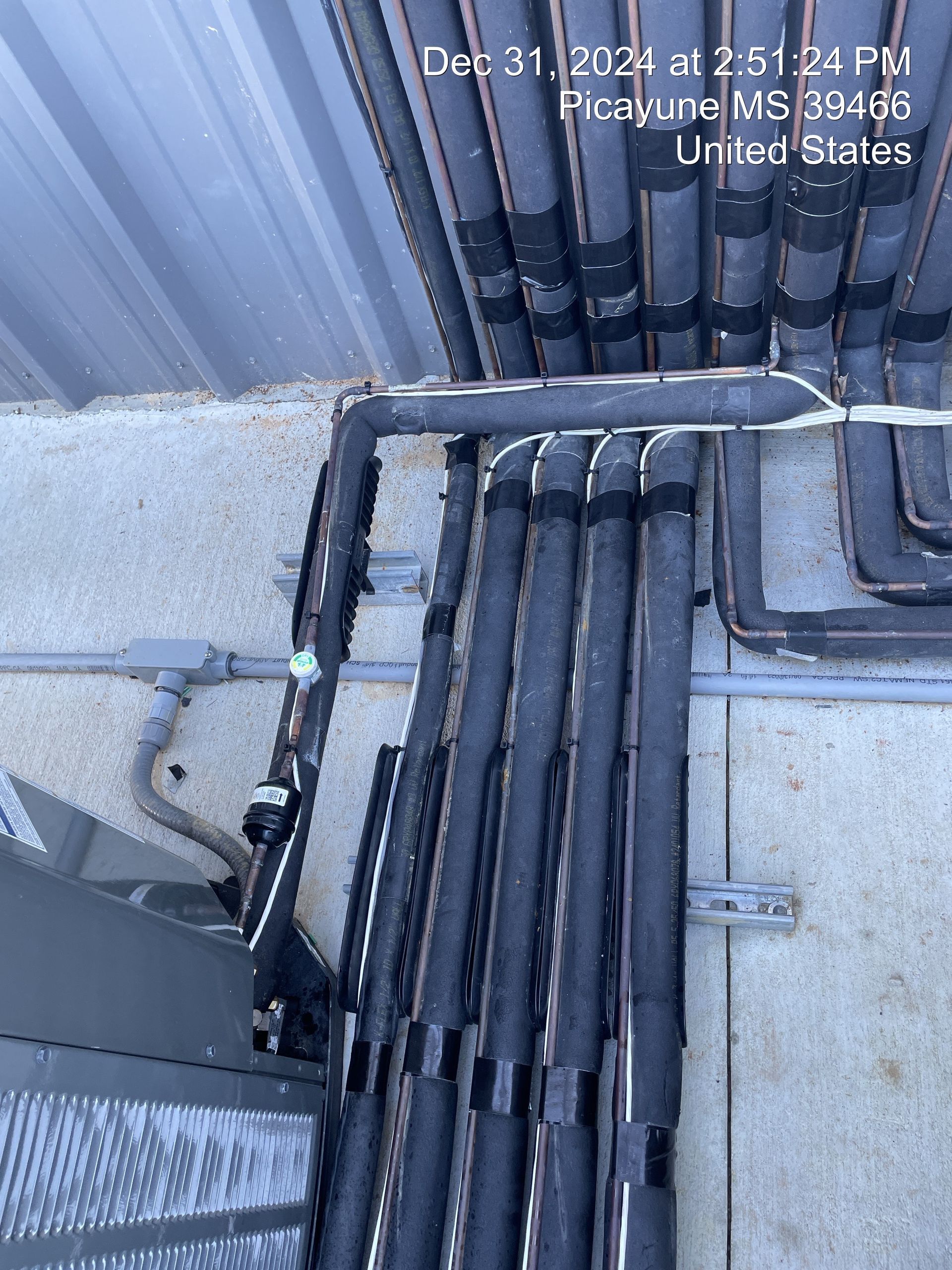 Bundle of black cables running along a rooftop beside a corrugated metal wall and concrete surface.
