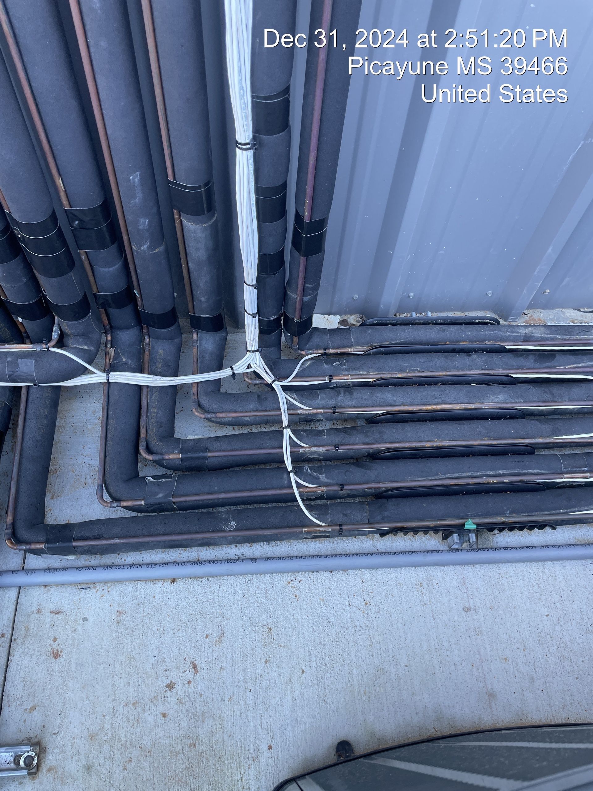 Close-up of bundled cables and conduit along a metal wall, with a concrete ledge below.