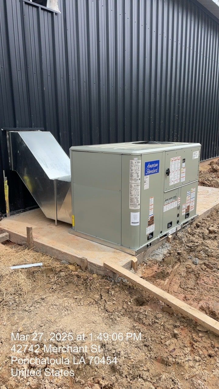 Outdoor HVAC unit beside a black metal building, with ductwork on a dirt foundation.