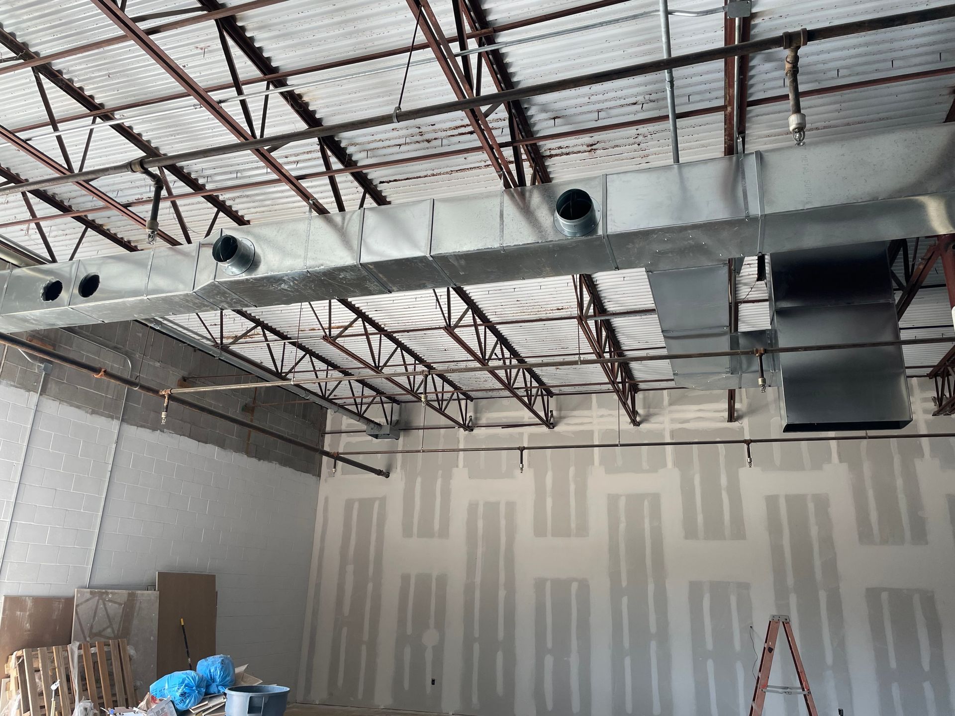 Interior construction site with exposed ceiling ducts, unfinished drywall, and a ladder against the wall