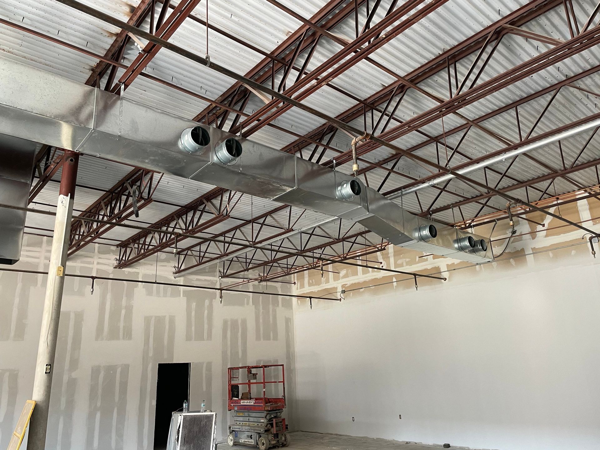 Empty warehouse interior with unfinished drywall, exposed ceiling beams, and ductwork.