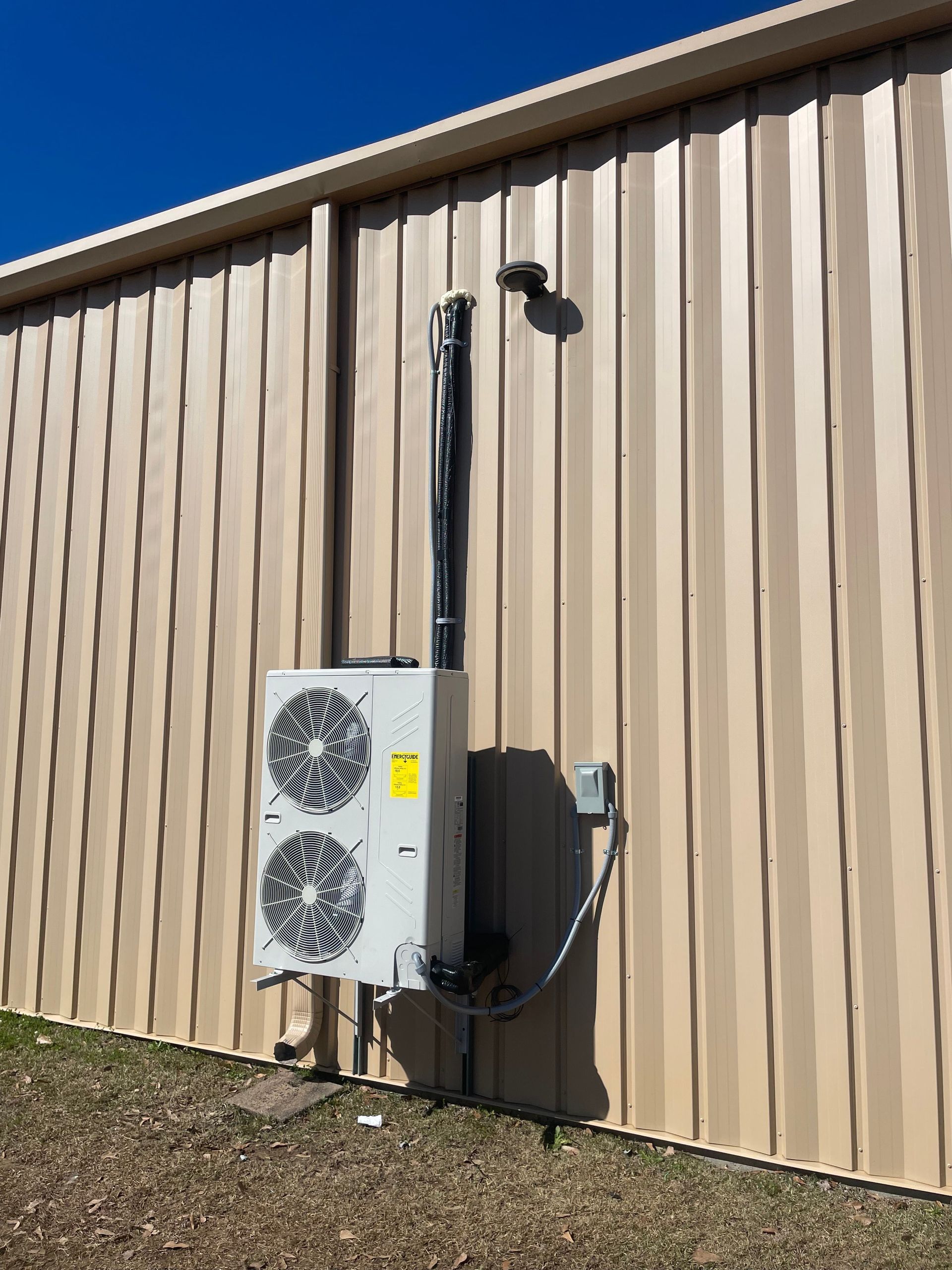 Outdoor HVAC unit mounted beside a tan metal building wall under a clear blue sky