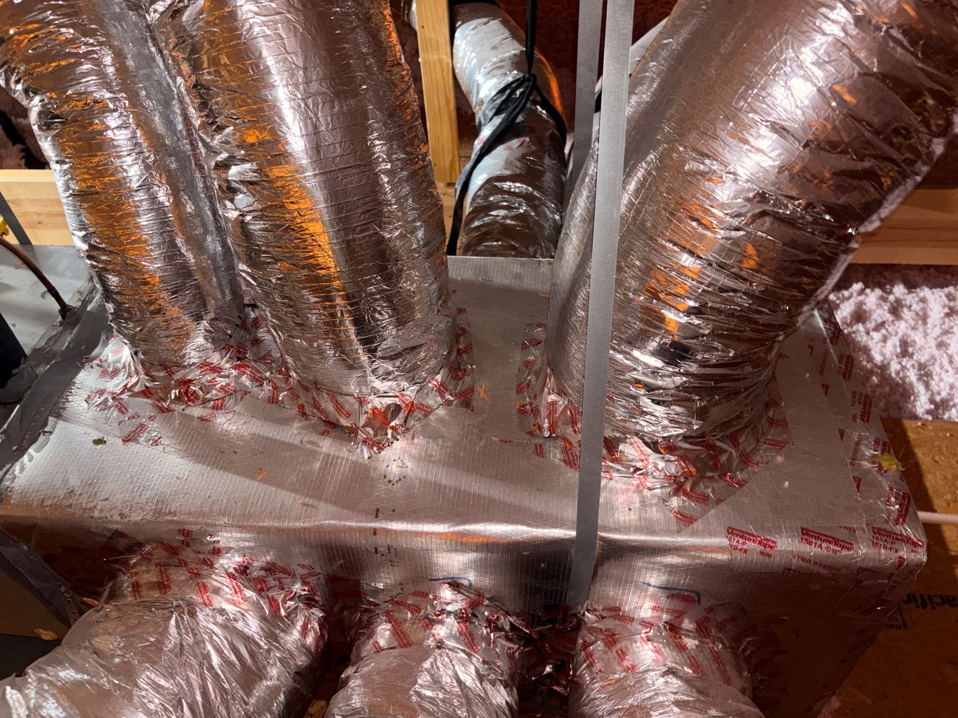 Foil-wrapped HVAC ducts branching from a central vent in a crawlspace or attic