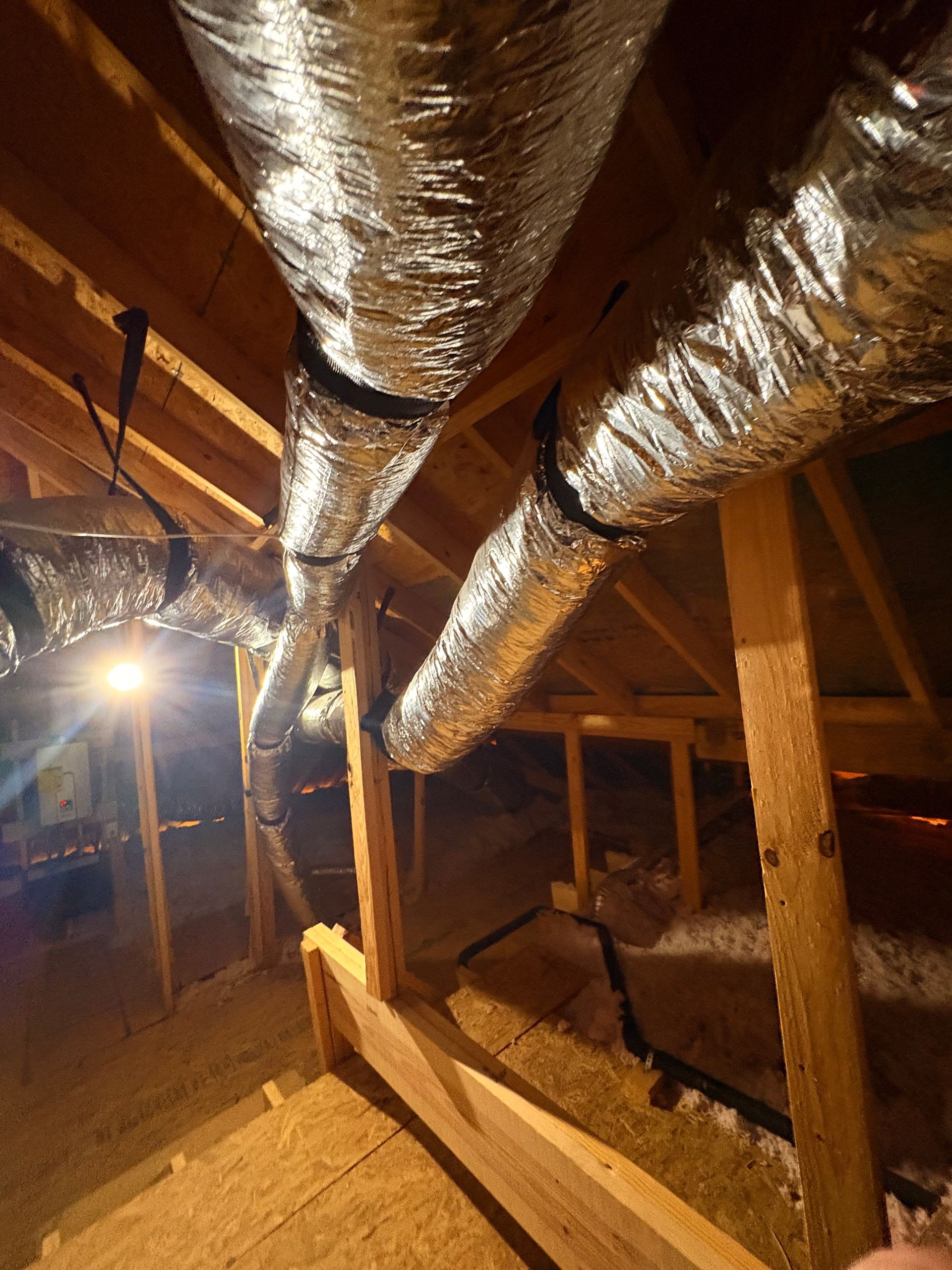 Crawlspace with insulated silver ductwork, exposed wooden beams, and dirt floor under a house.